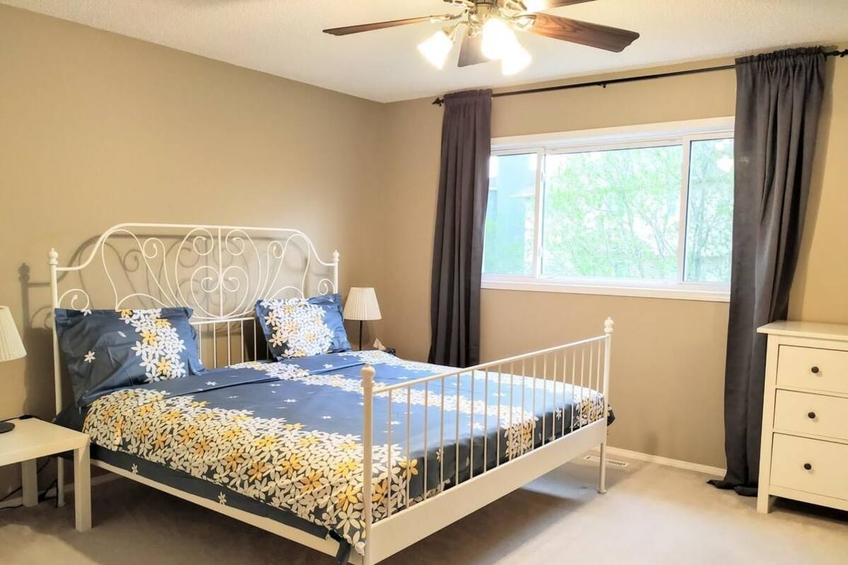 A bedroom with a metal bed frame, a window with curtains, a bedside table, and a nightstand.