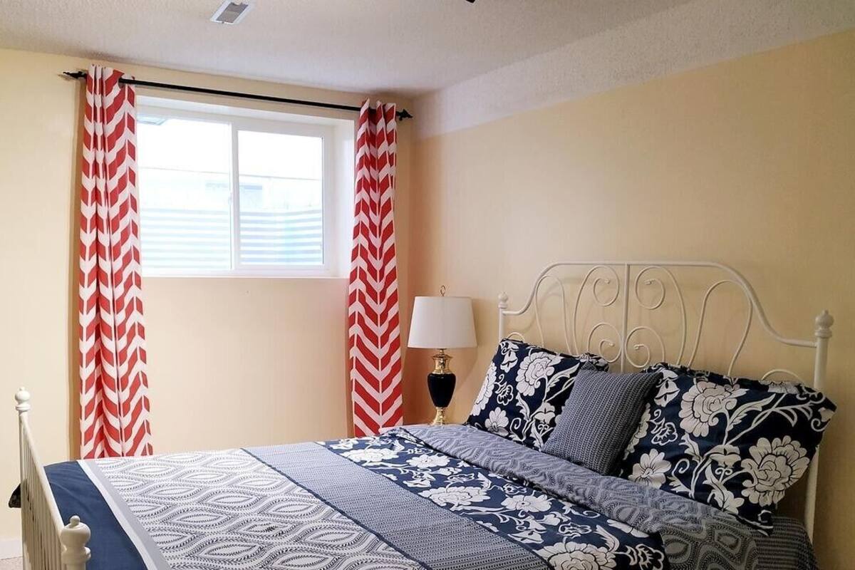 A bedroom with a bed, curtains, a lamp, and a window.
