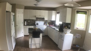 Una cocina con armarios blancos, salpicadero de azulejos, una isla central y una ventana con persianas.