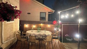 An outdoor patio with a round table and chairs, string lights, and a wooden bench.