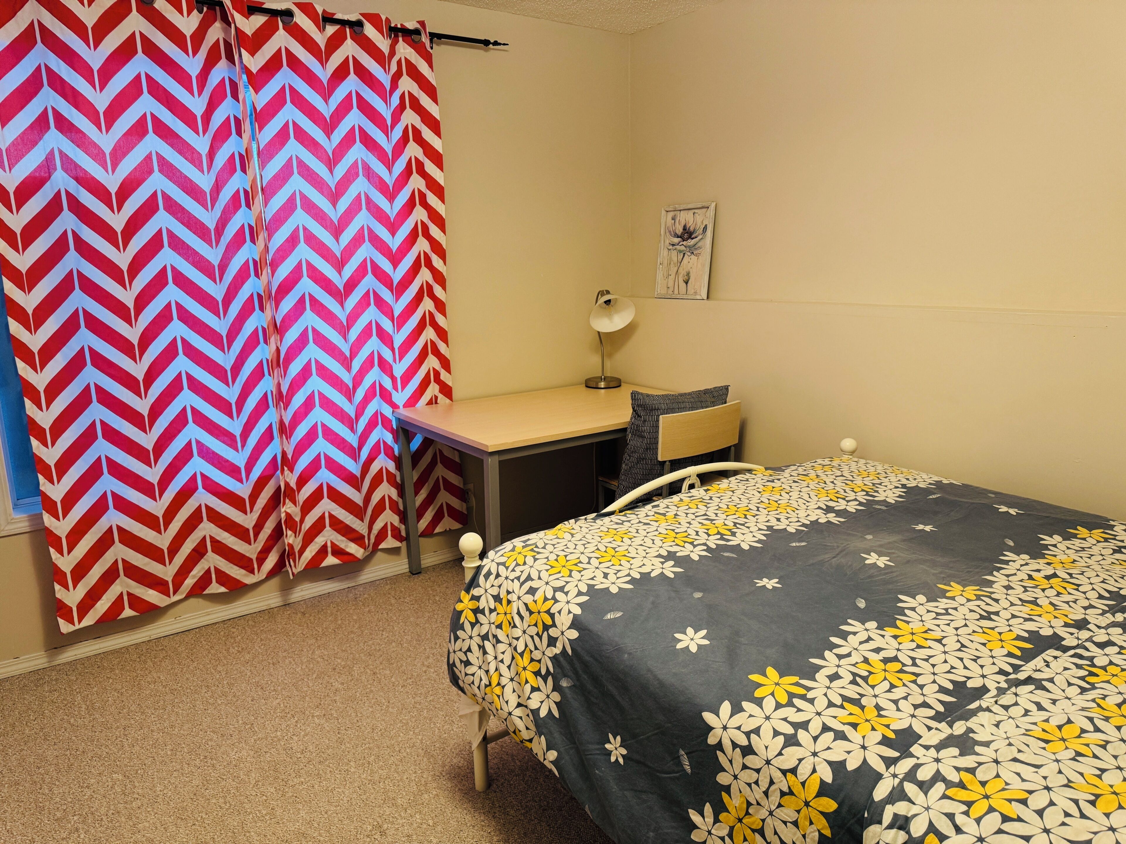 A bedroom with a bed, desk, chair, and a curtain.