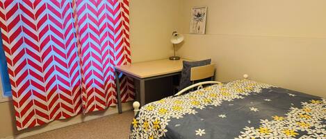 A bedroom with a bed, desk, chair, and a curtain.