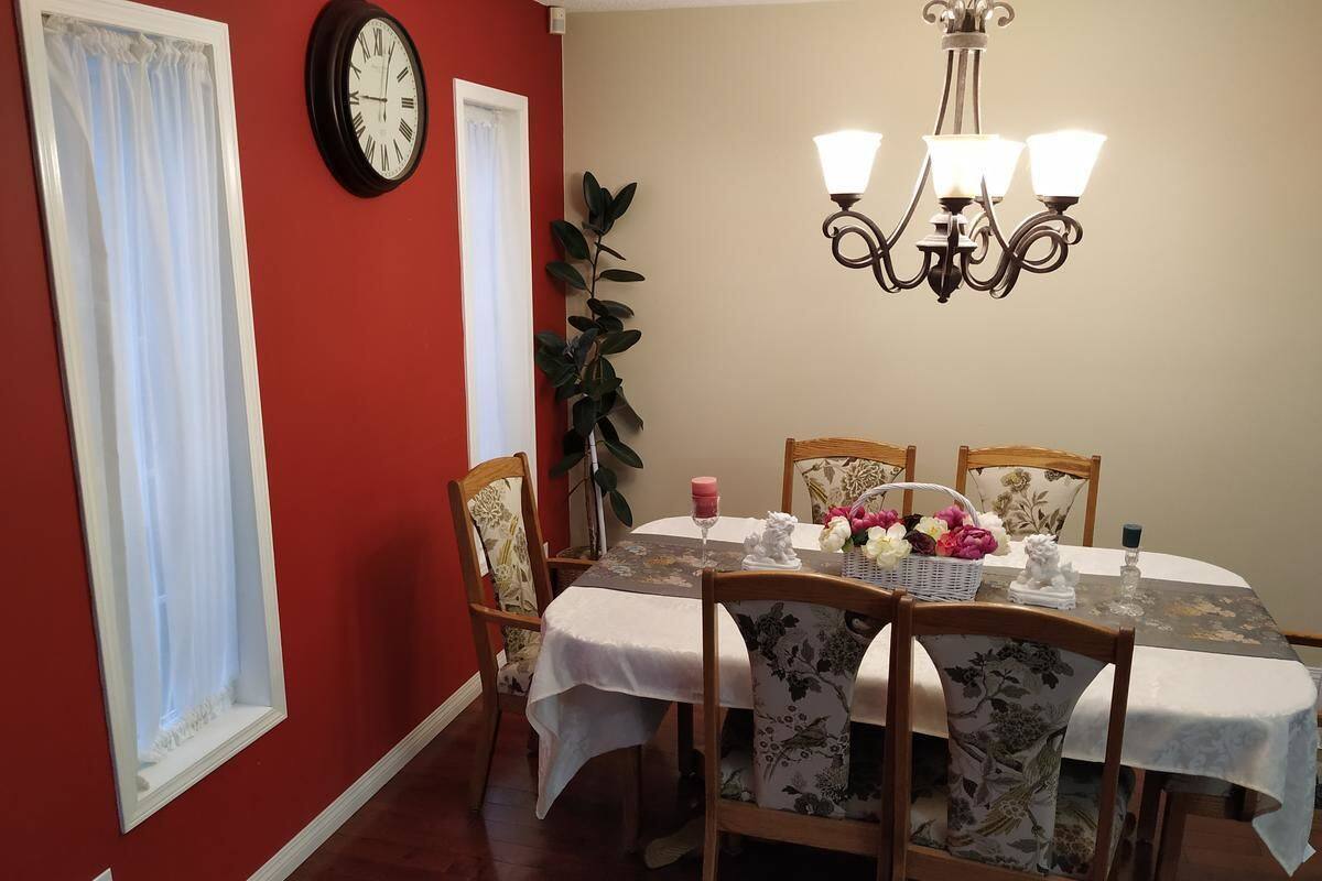 A dining room with a round table, chairs, a chandelier, a clock, and a plant.