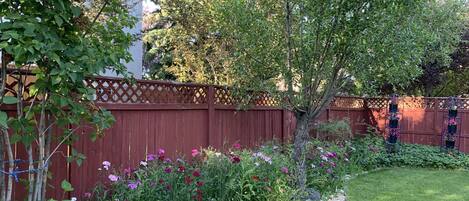 A garden with a wooden fence, a variety of flowering plants, and a small tree.