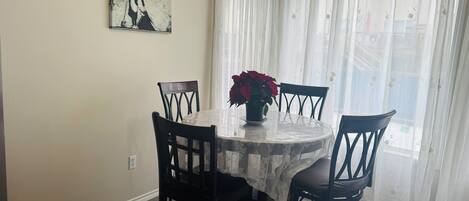 A dining area with a round table, four chairs, a vase with red flowers, and a painting on the wall.