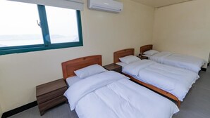 Habitación de hotel con tres camas individuales, una ventana con vistas, un equipo de aire acondicionado y una mesita de noche de madera.