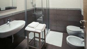 Een moderne badkamer met een douche met glazen wand, een wastafel, toilet en een bidet.