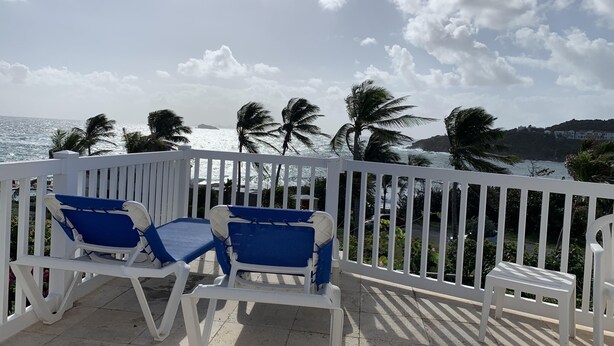 A balcony with white railings, two blue lounge chairs, and a view of the ocean and palm trees. - Paradise Villa Caribbean Ocean View (Philipsburg)