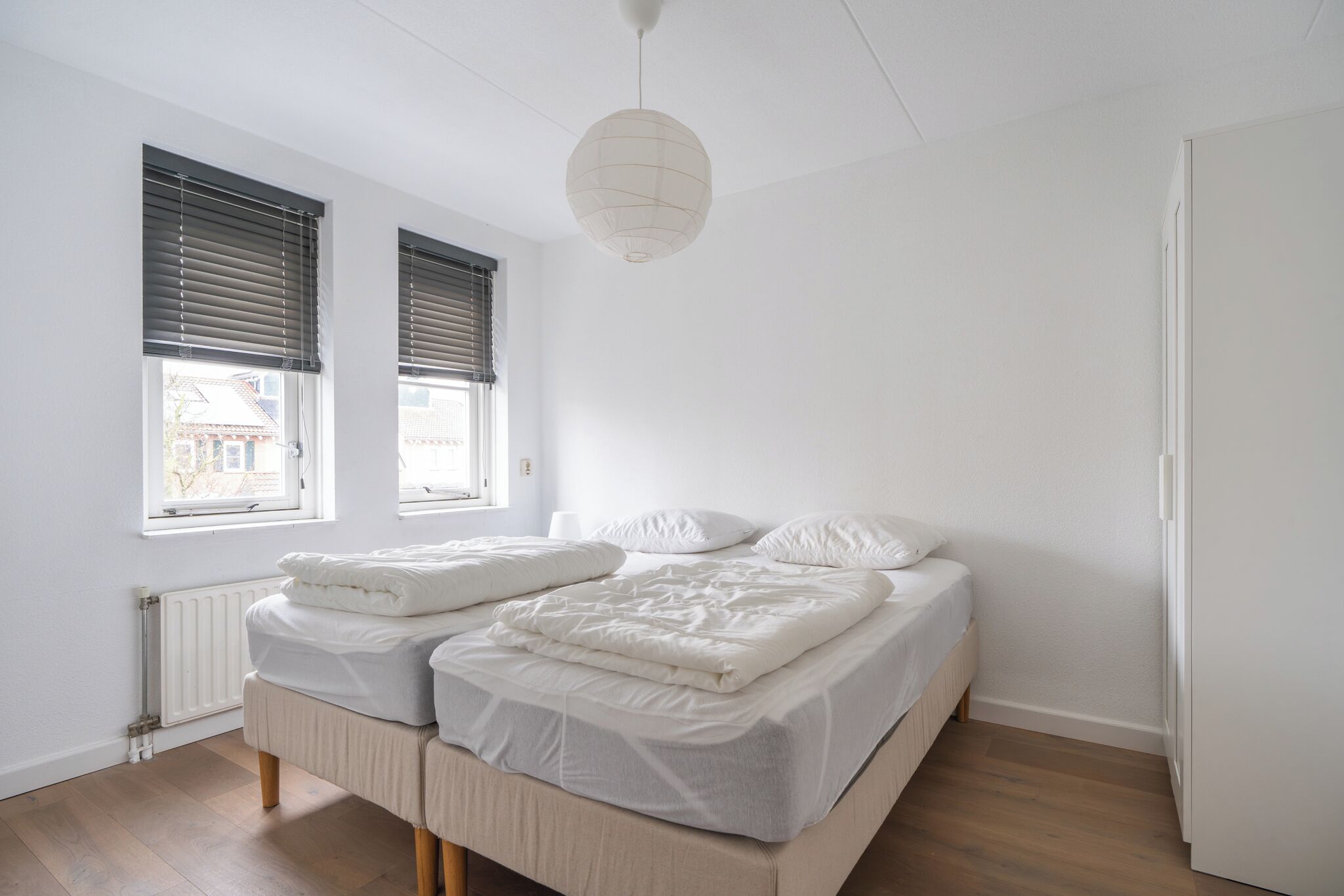 Une chambre avec deux lits, un radiateur et un luminaire suspendu.