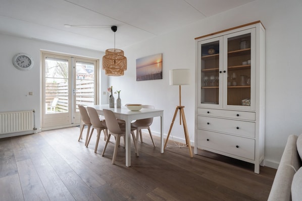 A dining area with a white table, chairs, and a lamp. There is a cabinet with glass doors and a clock on the wall.