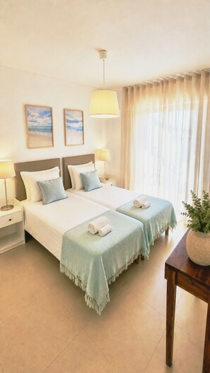 A hotel room with two beds, a bedside table, a lamp, a plant, and a window with curtains.