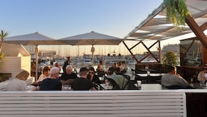 Un espace de restauration situé sur le toit, avec des places assises en plein air, des parasols et une vue sur les bateaux et les bâtiments.