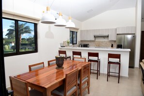 A modern kitchen with a central island, wooden dining table, and chairs. - Casa Boroda - Andromeda Pedasi - In Park with Swimming pool and Beach (Pedasi)