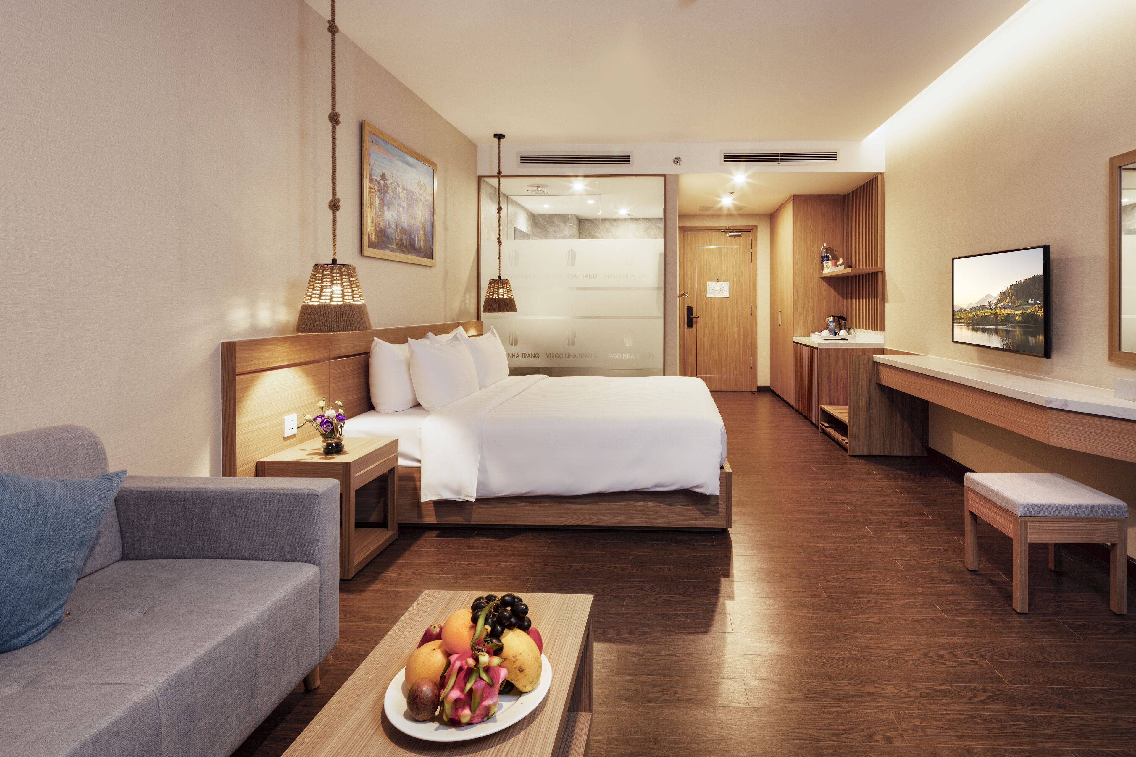Habitación de hotel con cama, sofá, escritorio y una mesa de comedor con fruta.