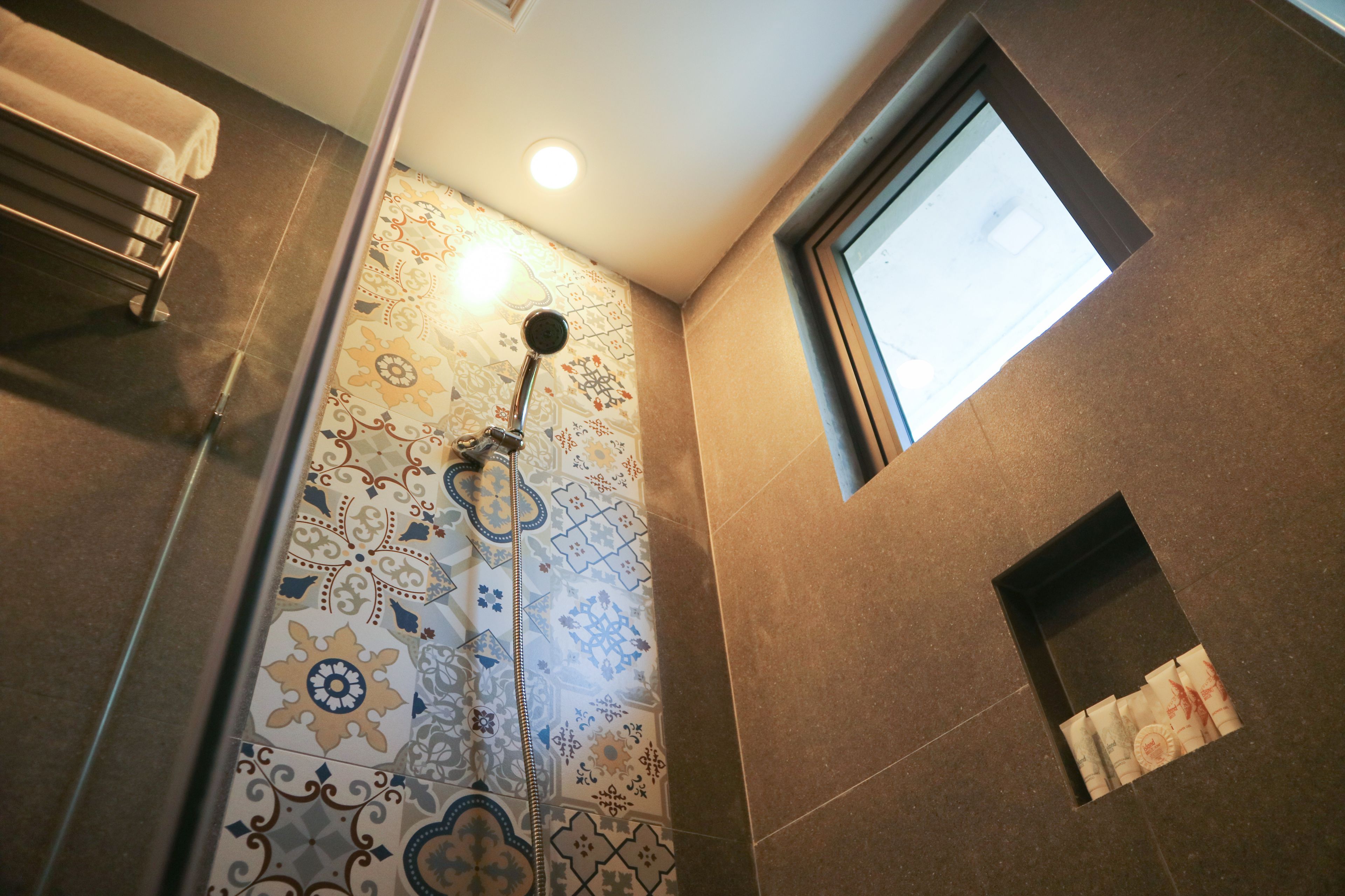 Una ducha con pared de azulejos estampados, un perchero y una ventana pequeña.