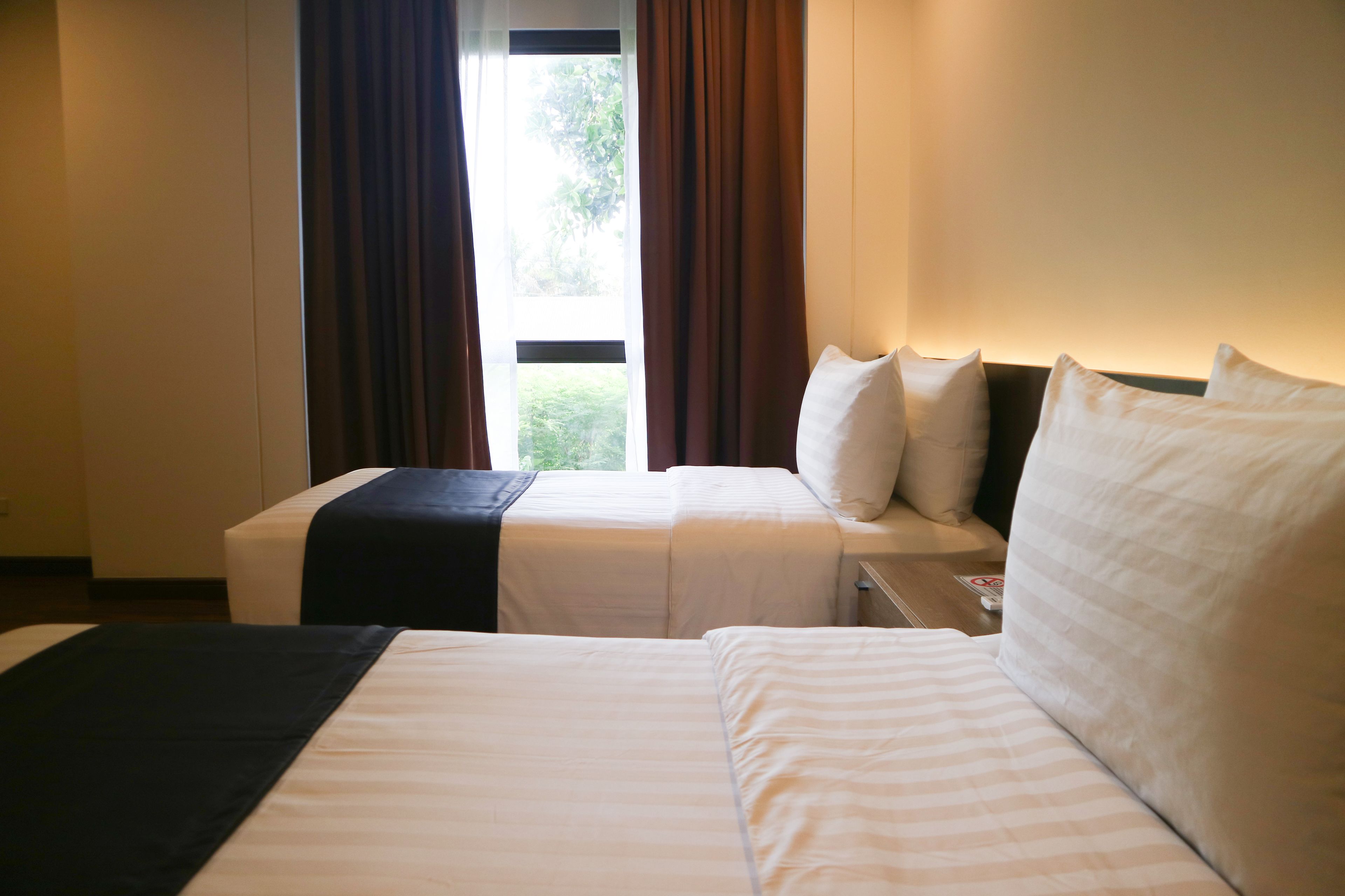 A hotel room with two beds, a window with curtains, and a bedside table.