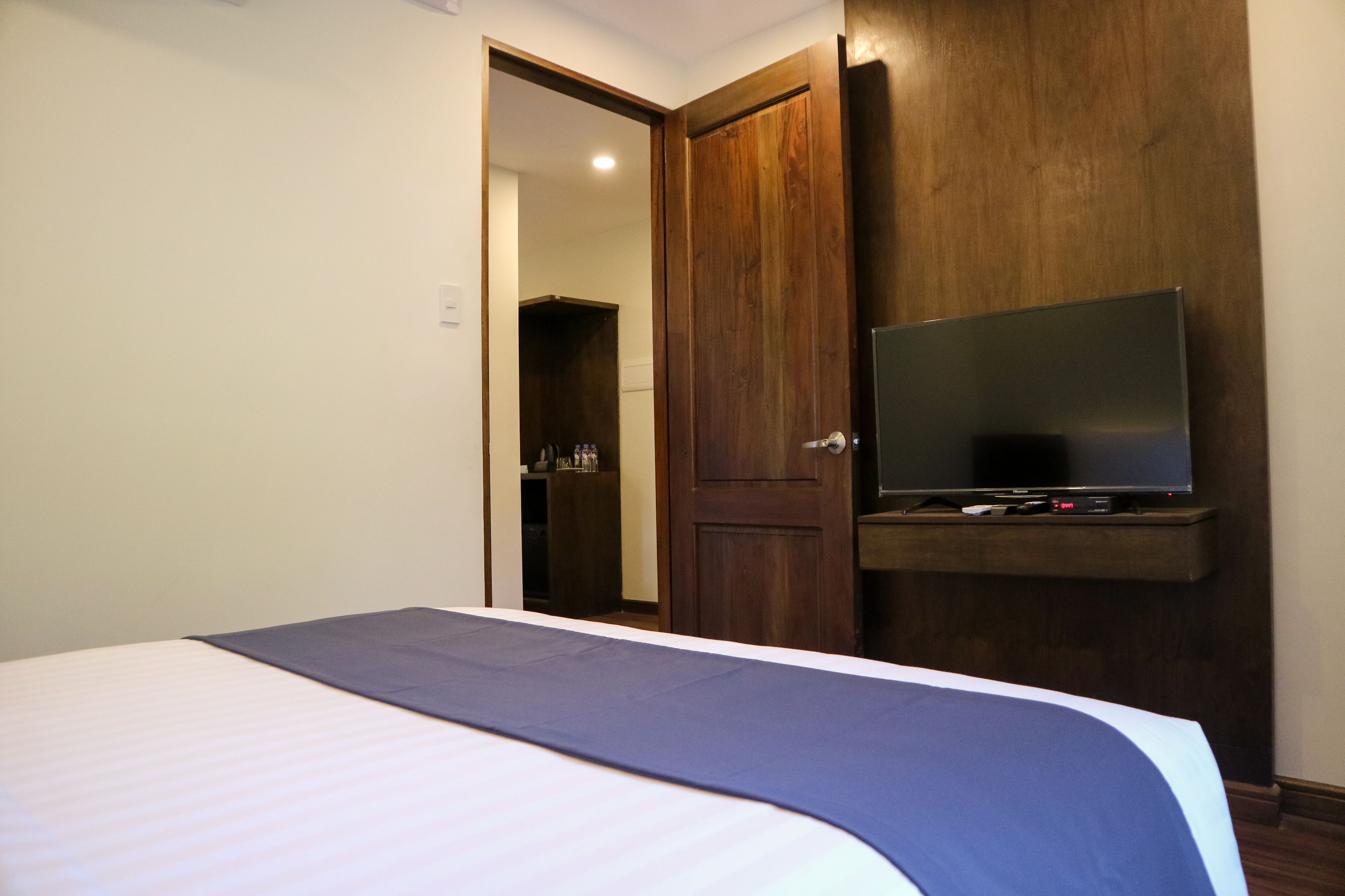 Una habitación de hotel con una cama, un televisor montado en la pared y un armario de madera.