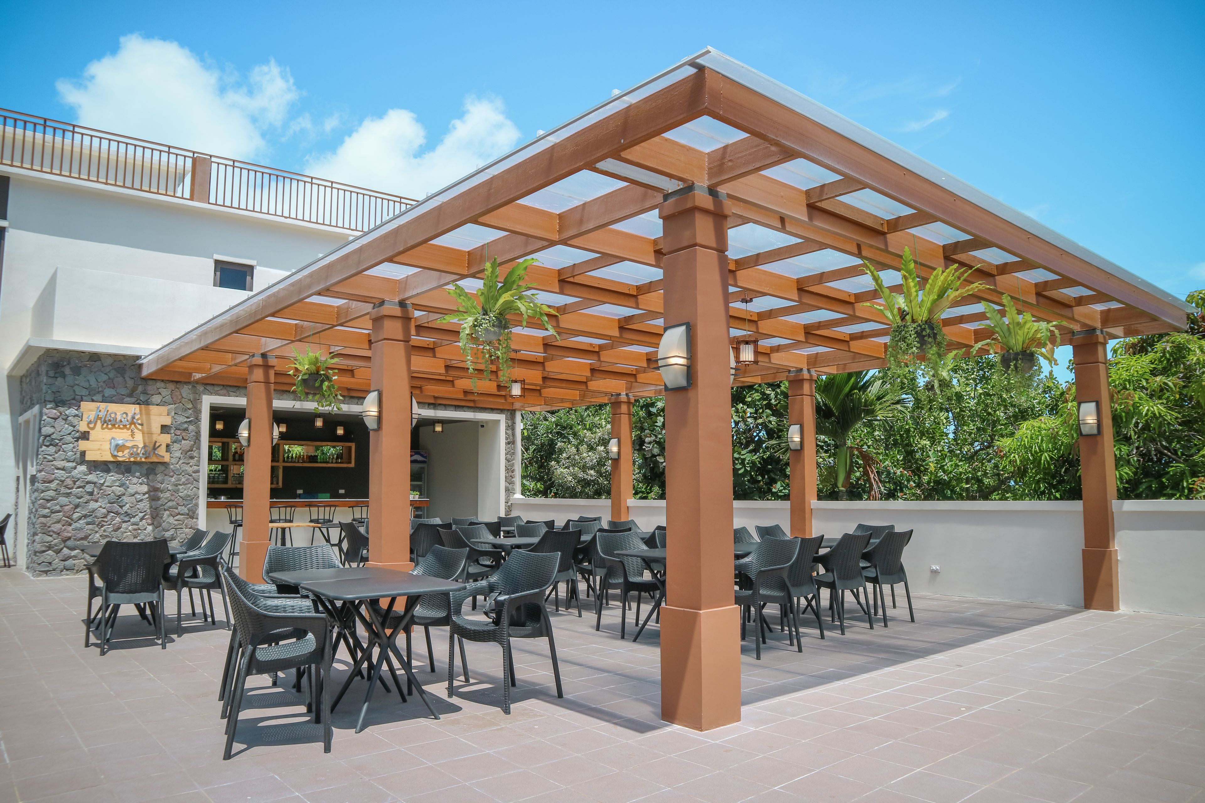 An outdoor patio with tables and chairs, a pergola, and a bar area with plants.