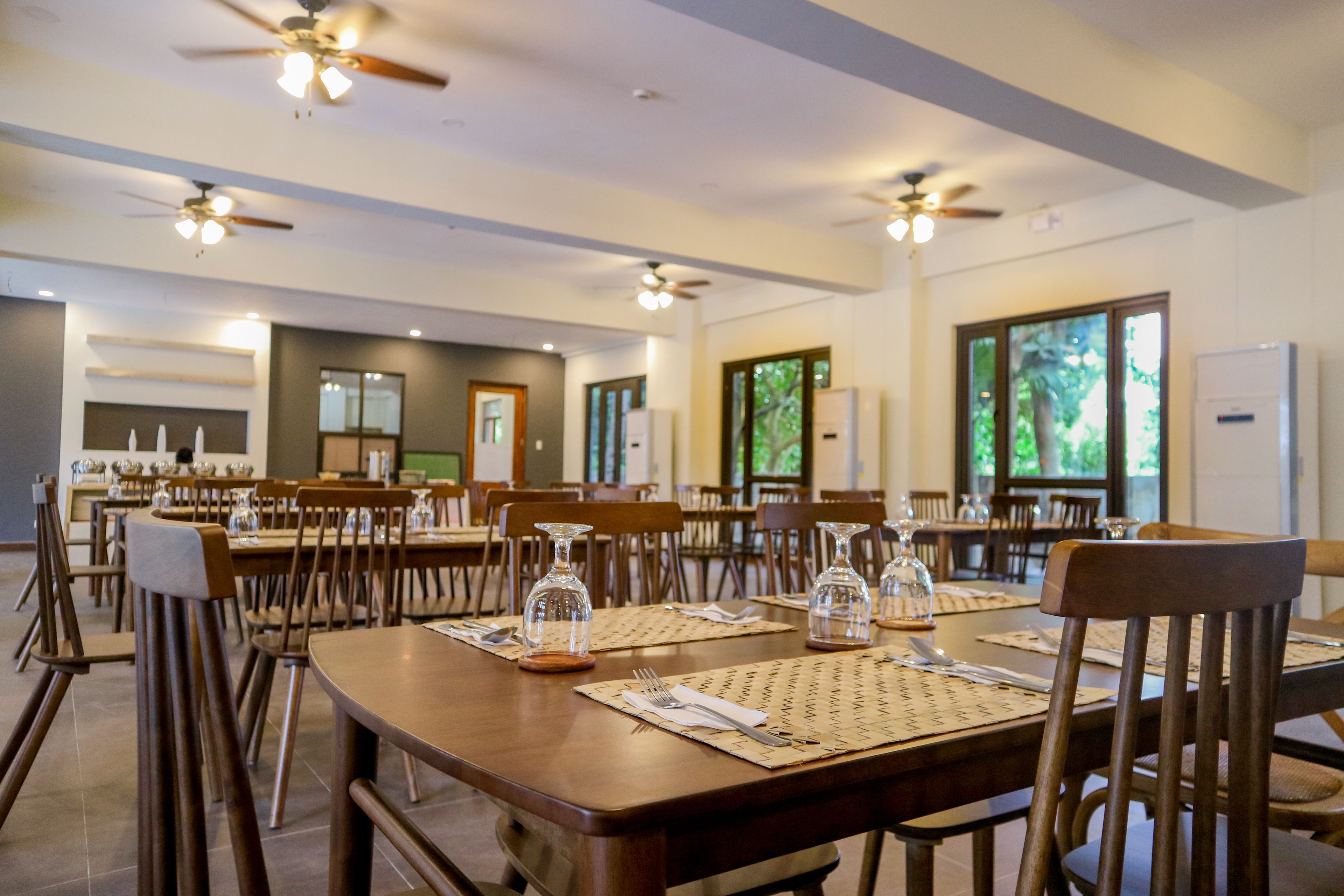 A dining area with multiple tables, chairs, ceiling fans, and large windows.