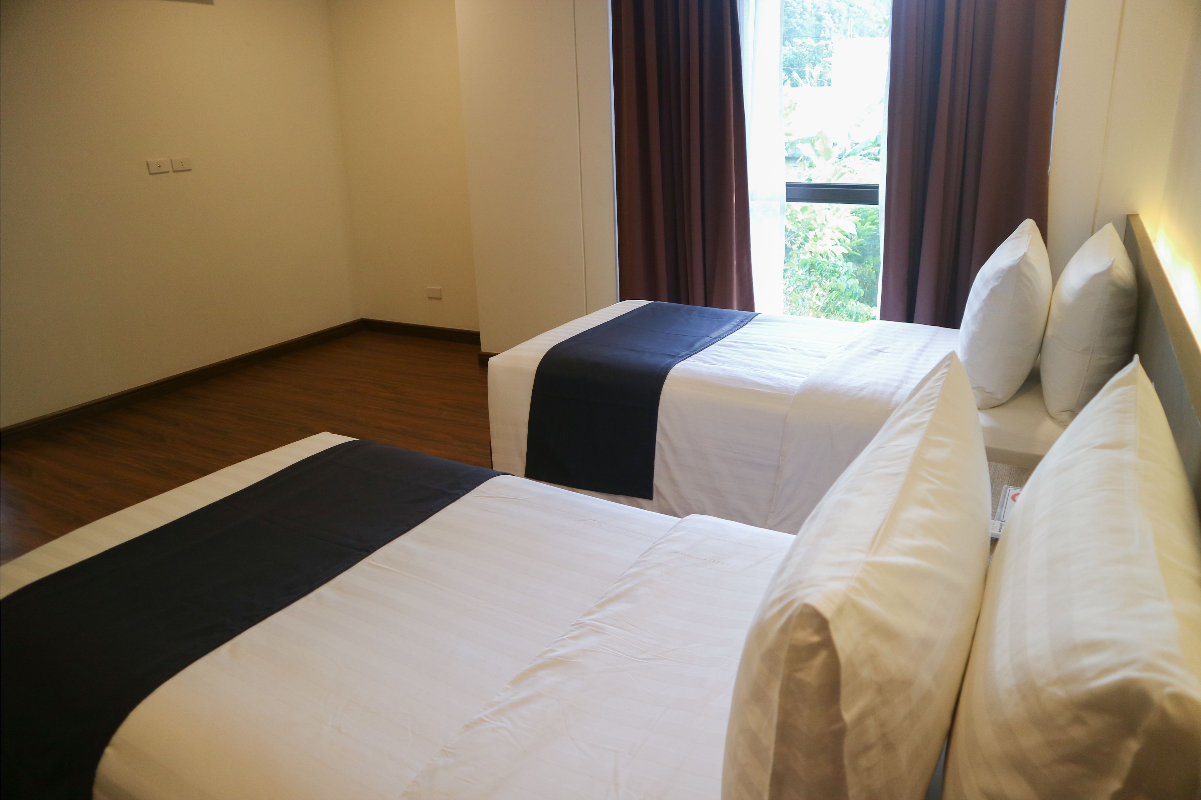A hotel room with two beds, a window with curtains, and a wooden floor.