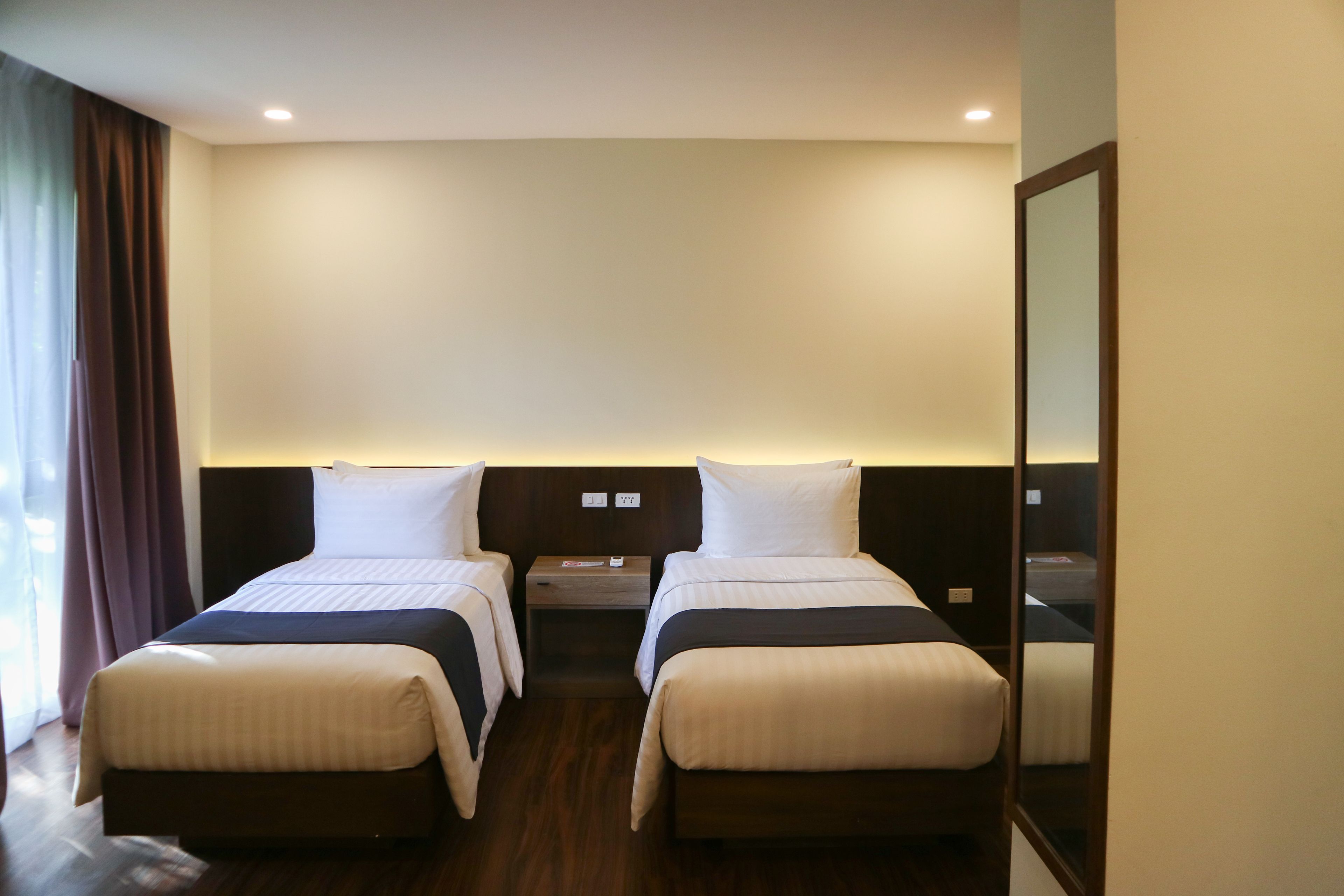 A hotel room with two beds, a nightstand, a mirror, and a window with curtains.