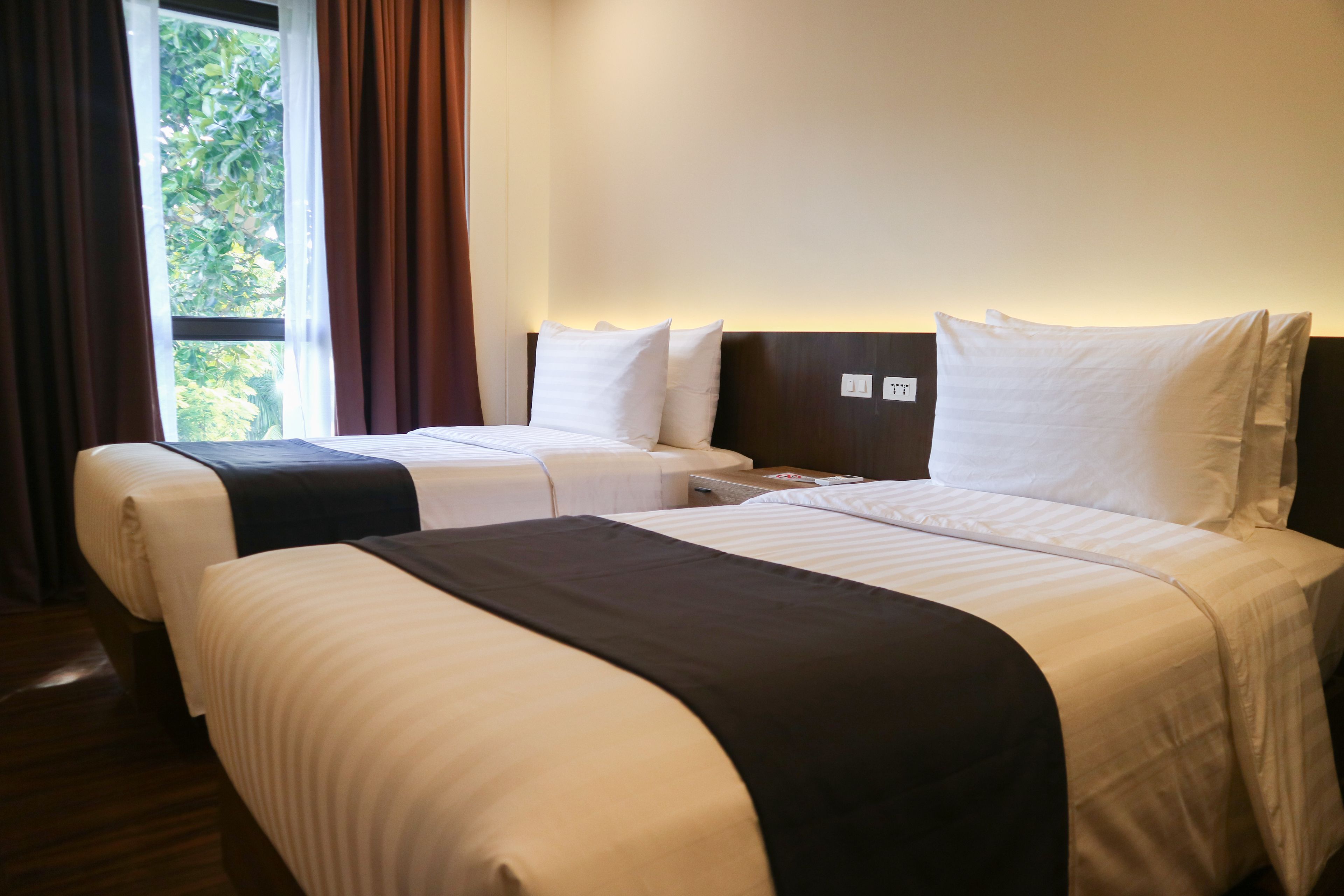 A hotel room with two beds, a nightstand, and a window with curtains.