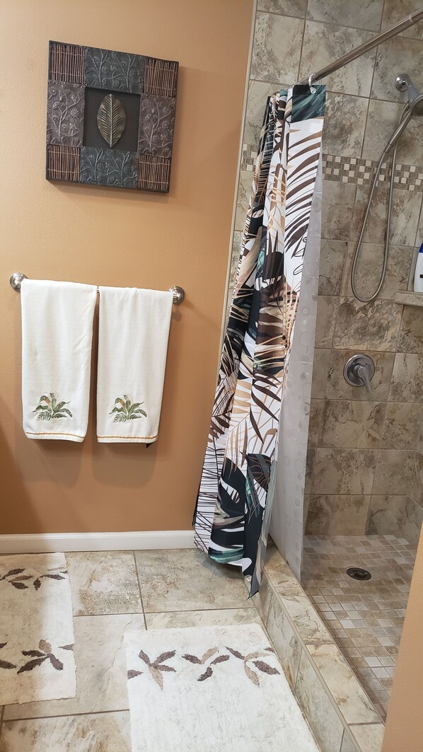 A bathroom with a shower, two towels, a decorative wall piece, and patterned floor mats.