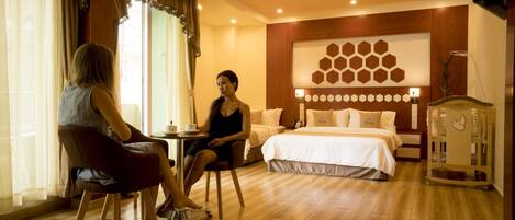 Une chambre d’hôtel avec un lit, une petite table et une chaise. Il y a une fenêtre avec des rideaux, un mur orné d’un motif hexagonal et un ventilateur de plafond.