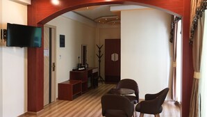 A modern living room with a wooden archway, a flat-screen TV mounted on the wall, a small table with chairs, and a coat rack. - Rosemary Boutique (Maafushi)