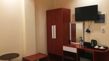 Een hotelkamer met een houten garderobe, een bureau met spiegel, een aan de muur bevestigde televisie en een klein tafeltje met prullenbak.