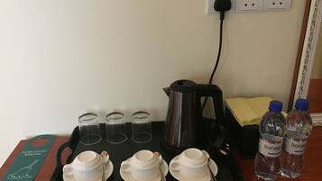 Una bandeja con tres tazas y platillos blancos, una tetera eléctrica negra, cuatro vasos de vidrio transparentes y dos botellas de agua sobre una mesa de madera.