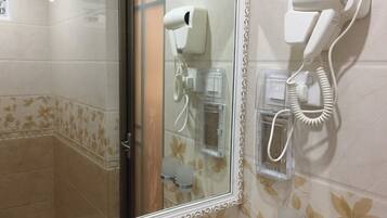A bathroom with a glass-enclosed shower, a hairdryer mounted on the wall, and a towel rack.
