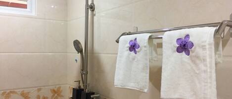 Une salle de bain avec une douche, un porte-serviettes avec deux serviettes et des carreaux décoratifs sur les murs.