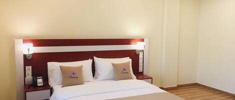 Una cama bien hecha con ropa de cama blanca y beige, un cabecero de madera y lámparas de noche.