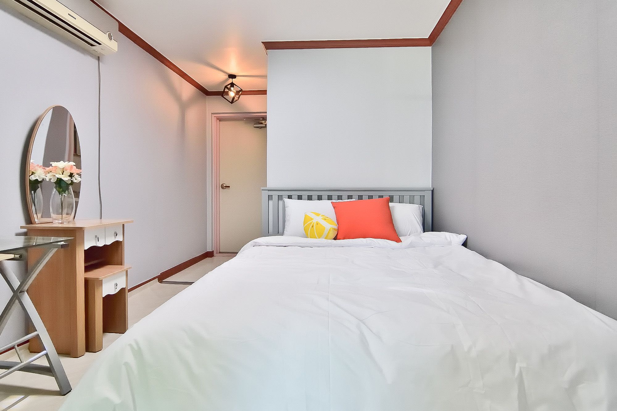 Et soveværelse med seng, kommode, spejl og loftlampe.