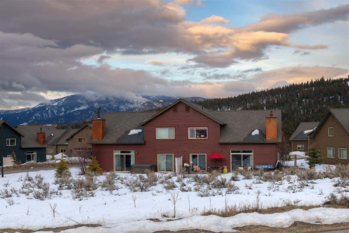 Un quartier résidentiel avec des maisons, un bâtiment rouge doté d’une cheminée, et un paysage enneigé avec des montagnes en arrière-plan.