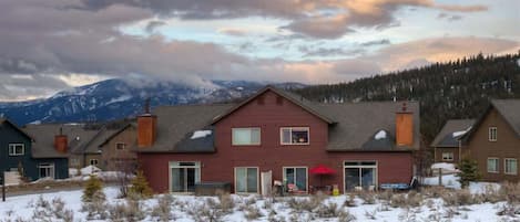 Una zona residencial con casas, un edificio rojo con chimenea y un paisaje nevado con montañas al fondo.