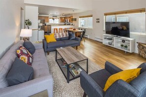 A modern living room with a grey sofa, a coffee table, and a TV stand. - Beautiful Firelight Chalet-Big Sky Town Center (Big Sky)