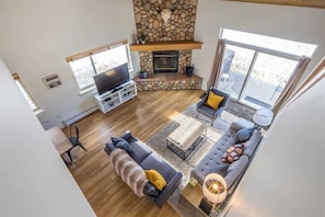 Un salón amplio con chimenea de piedra, televisor de pantalla plana y un ventanal con vistas al exterior.