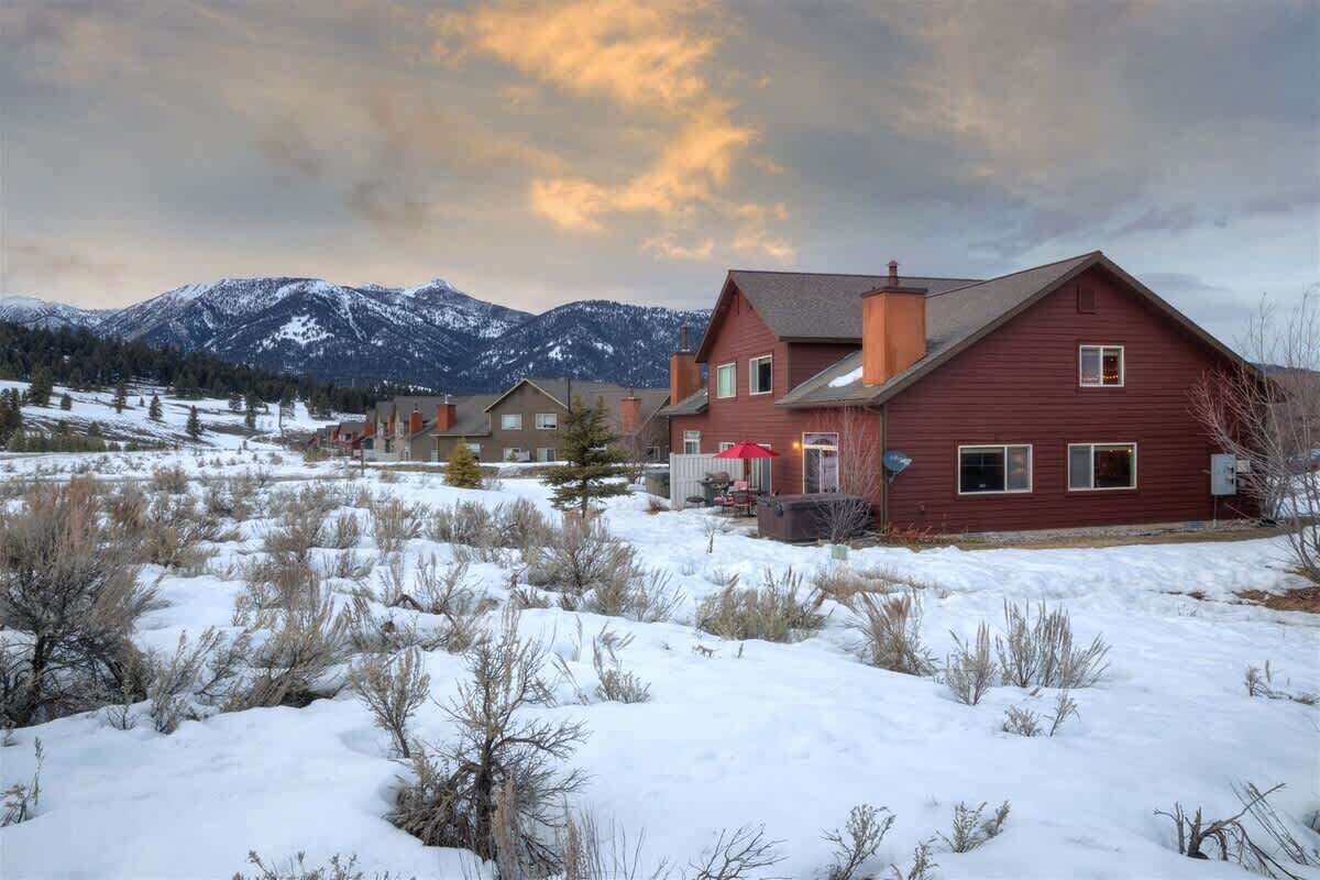 Una casa roja con chimenea, rodeada de nieve y montañas al fondo.