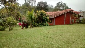 A red brick house with a tiled roof, surrounded by a well-maintained lawn and various plants.