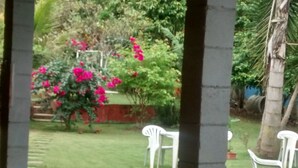 A garden with a lawn, white plastic chairs, and a red wall.