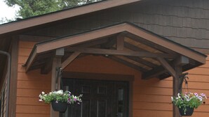 A wooden house with a dark brown door, stone pillars, and hanging flower baskets. - Luxury Guest House With River Access  (Bigfork)