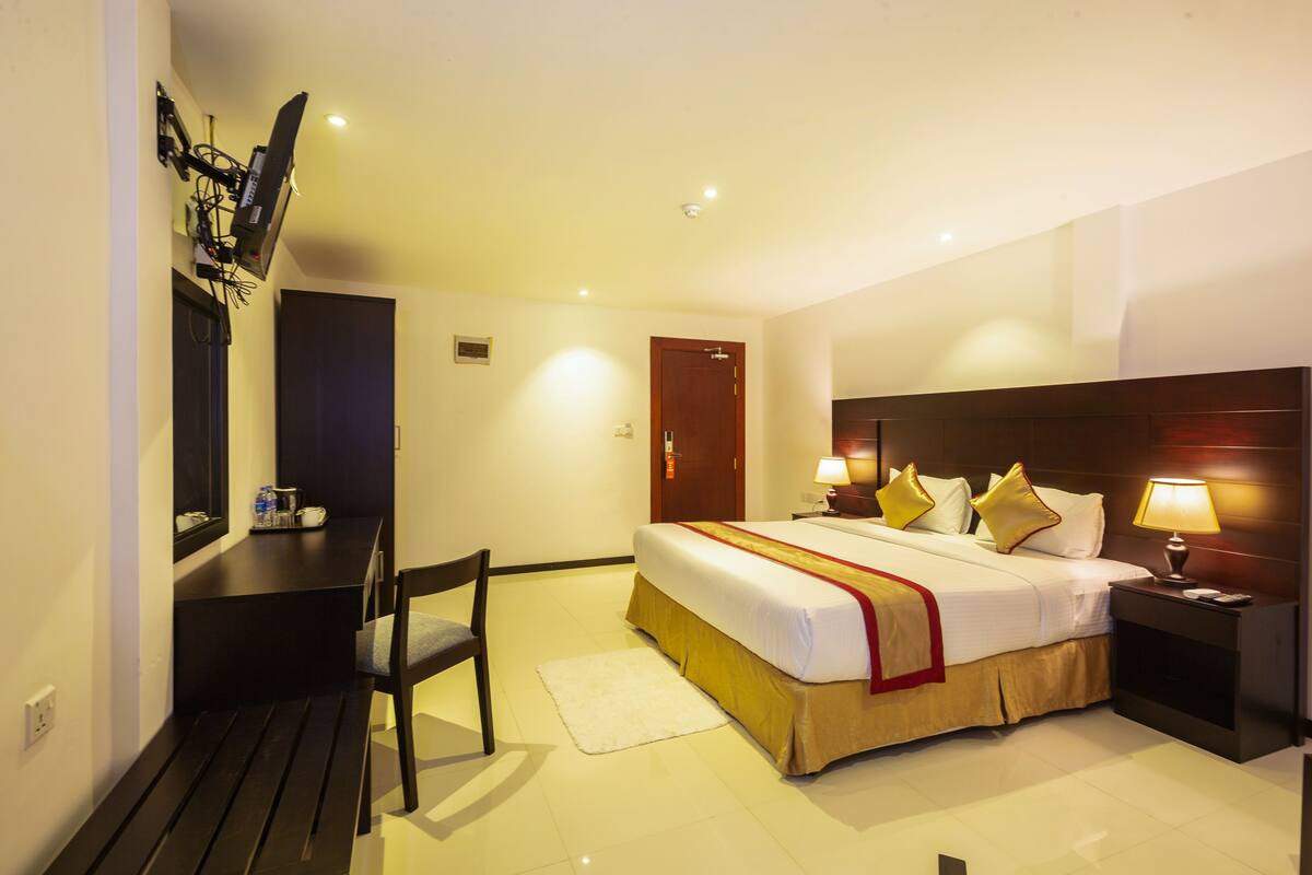 A hotel room with a bed, bedside tables, a desk, a chair, and a television mounted on the wall.