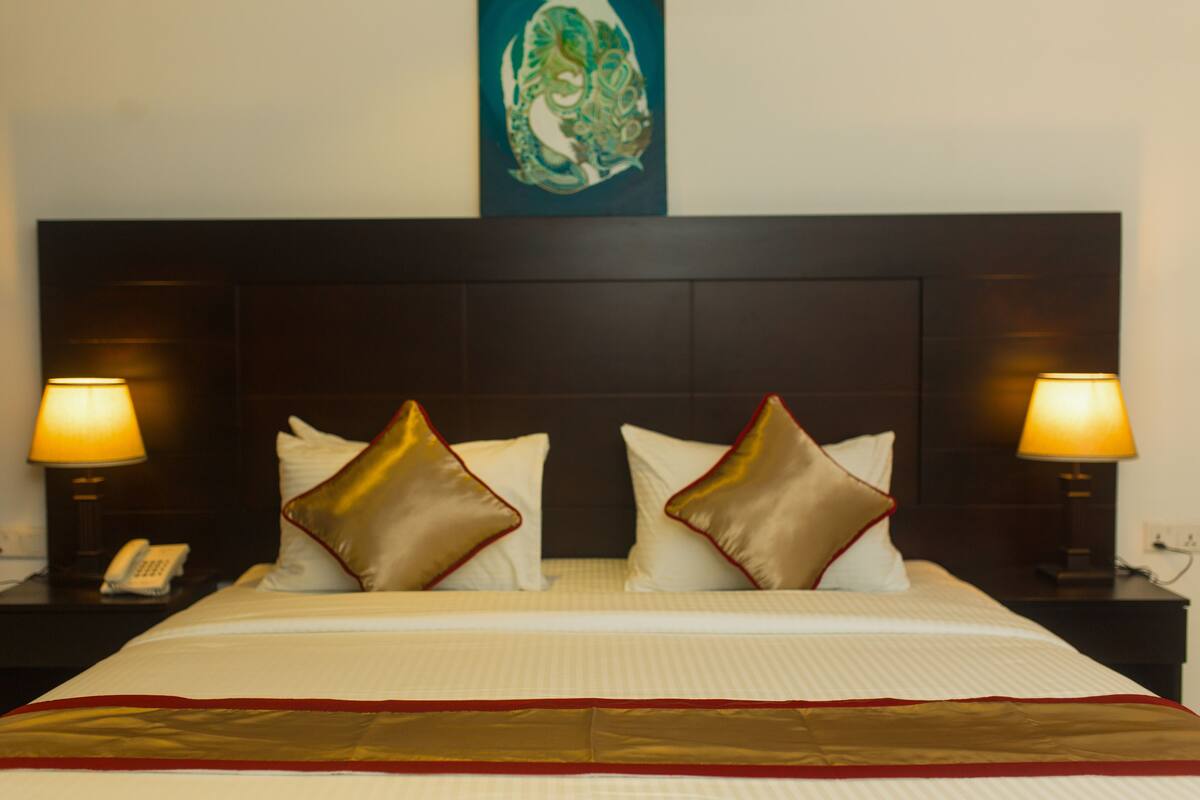 A hotel room with a large bed, two bedside lamps, a telephone, and a decorative wall piece above the bed.