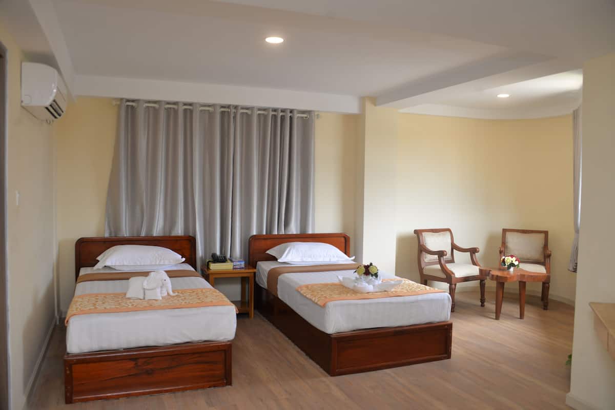 A hotel room with two wooden beds, a nightstand, a chair, and a small table with a vase of flowers.