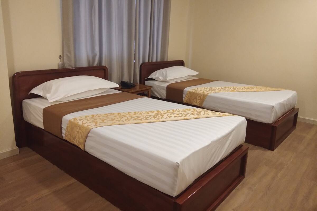 A hotel room with two wooden beds, each with white linens and a brown decorative runner.