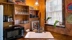 A kitchen with wooden shelves, a sink, a microwave, and a window with blinds. - The Cottage - 2 miles to I-65 (Montevallo)