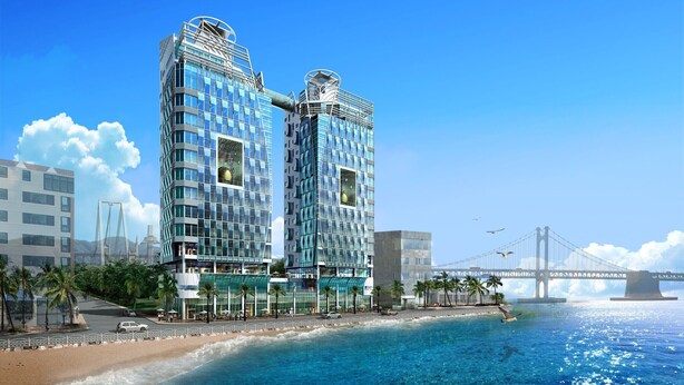Hotel moderno com fachada de vidro, próximo a uma praia e uma ponte.
