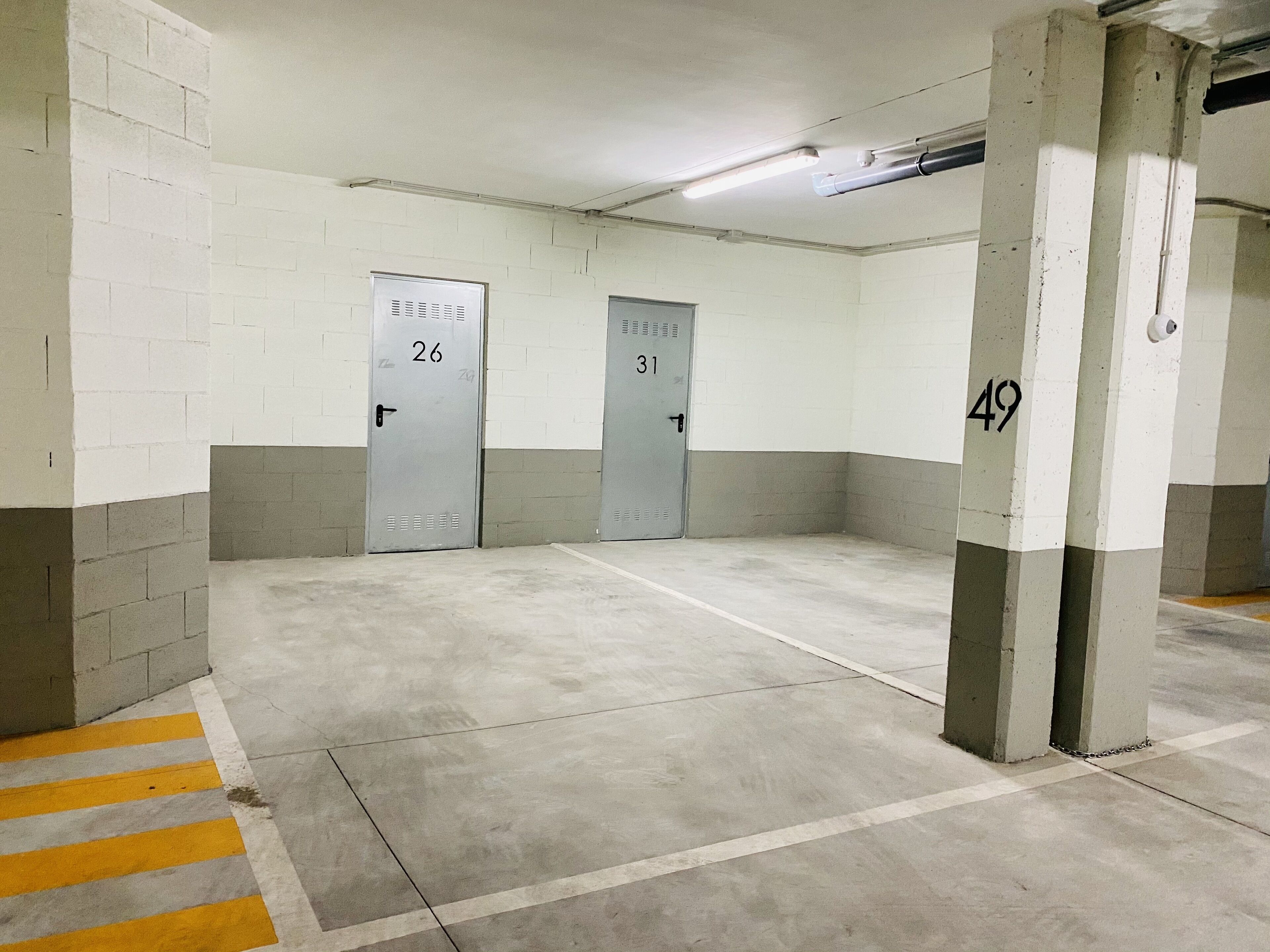 Een parkeergarage met betonnen vloeren en muren, gemarkeerde parkeerplaatsen en genummerde garagedeuren.